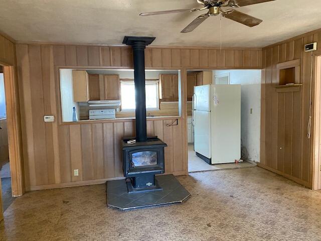 unfurnished living room with a wood stove, wood walls, ceiling fan, and light carpet