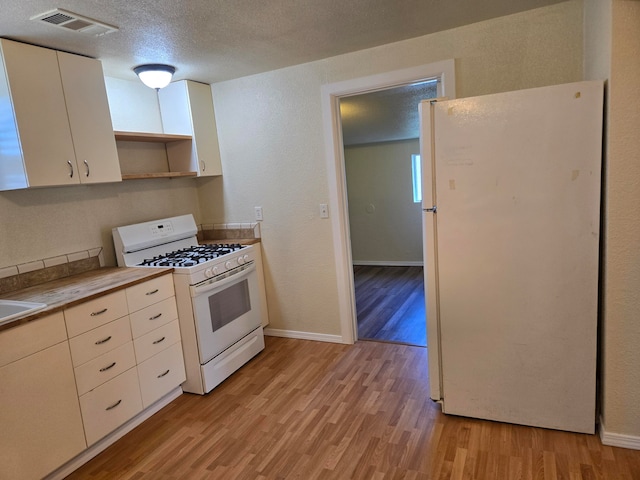 kitchen with a textured ceiling, white appliances, and light wood-type flooring