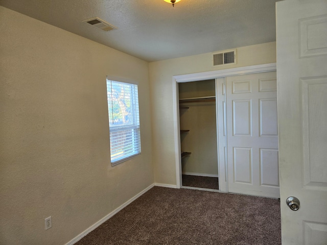 unfurnished bedroom with a closet, a textured ceiling, and dark colored carpet