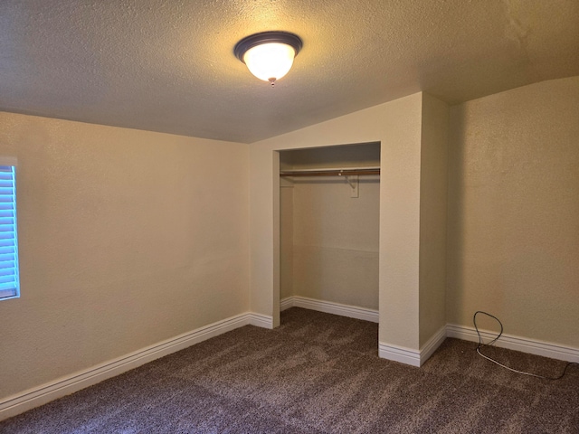 unfurnished bedroom with a textured ceiling, a closet, lofted ceiling, and dark colored carpet