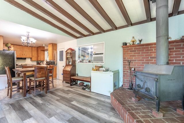 dining space featuring a chandelier, vaulted ceiling with beams, hardwood / wood-style flooring, and a wood stove