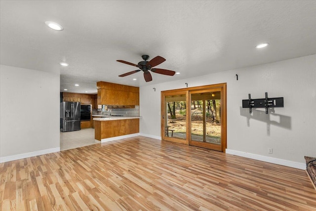 unfurnished living room with ceiling fan, a textured ceiling, and light hardwood / wood-style flooring