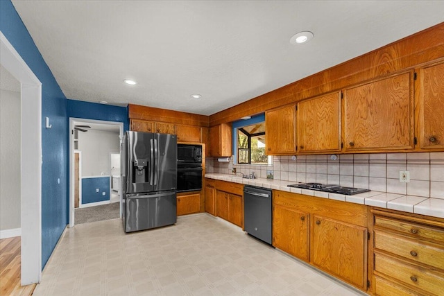 kitchen featuring tile countertops, decorative backsplash, sink, and black appliances