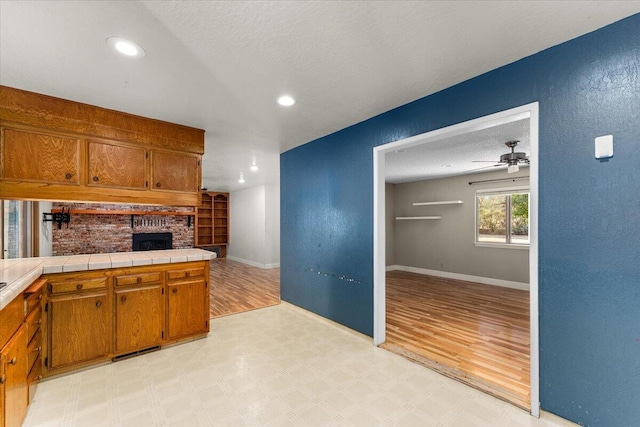 kitchen with ceiling fan, tile counters, a textured ceiling, and light wood-type flooring