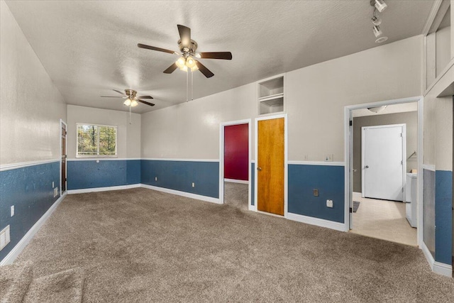 carpeted empty room featuring ceiling fan, track lighting, a textured ceiling, and washer / dryer