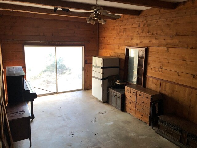 unfurnished living room with concrete flooring, wood walls, beamed ceiling, and ceiling fan