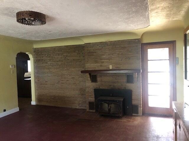 unfurnished living room featuring a wood stove, baseboards, arched walkways, and a textured ceiling