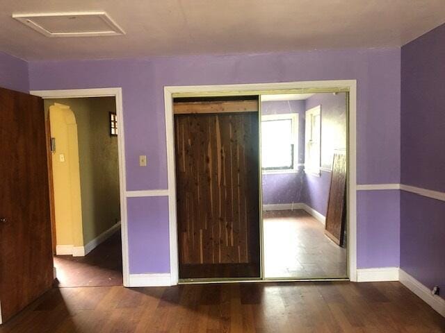 empty room with arched walkways, wood finished floors, attic access, and baseboards