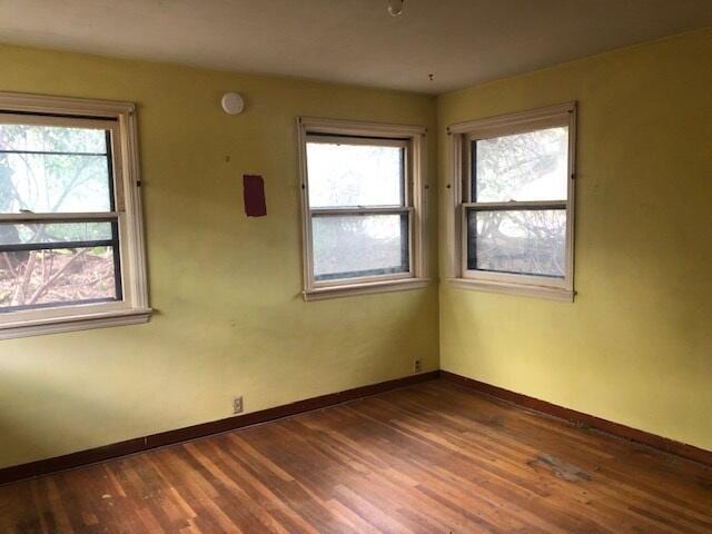 unfurnished room with plenty of natural light, wood finished floors, and baseboards