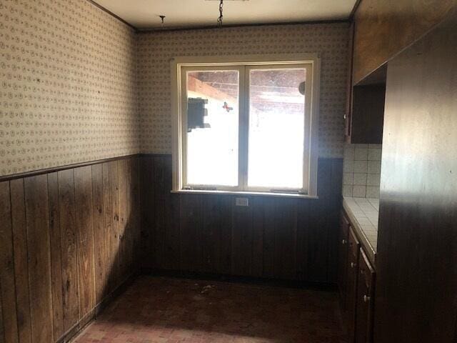 interior space featuring a wainscoted wall, wooden walls, brick floor, and wallpapered walls