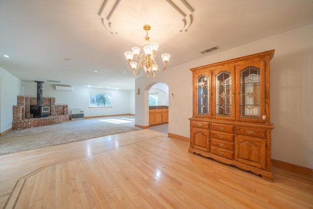 unfurnished dining area featuring a notable chandelier, light wood-type flooring, a wood stove, and a wall unit AC