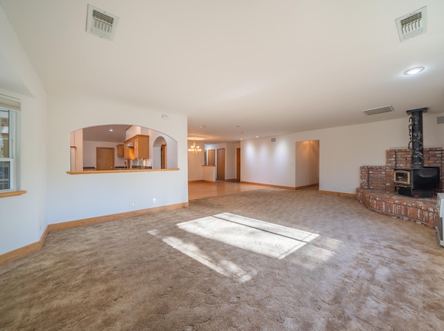 unfurnished living room with carpet flooring, a wood stove, and a chandelier