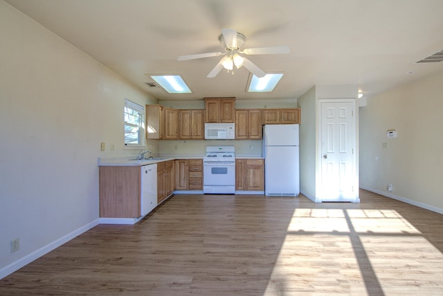 kitchen featuring a skylight, white appliances, ceiling fan, sink, and light hardwood / wood-style floors