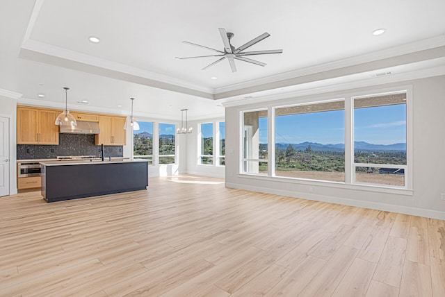 unfurnished living room featuring a mountain view, ceiling fan with notable chandelier, sink, light wood-type flooring, and ornamental molding