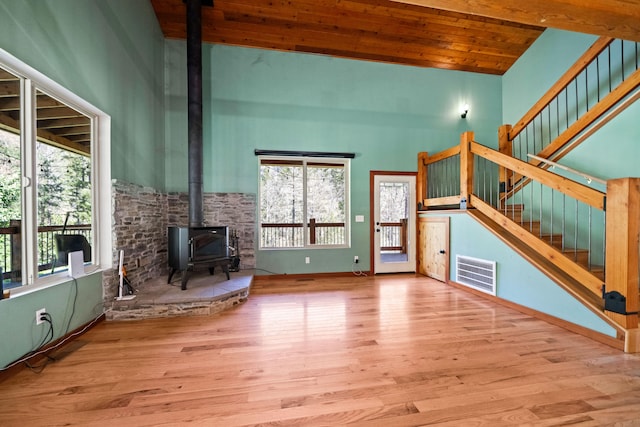 unfurnished living room with beam ceiling, a wood stove, high vaulted ceiling, light hardwood / wood-style floors, and wood ceiling