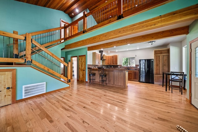 unfurnished living room featuring sink, beam ceiling, high vaulted ceiling, wooden ceiling, and light hardwood / wood-style floors