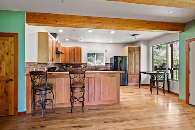 kitchen with backsplash, black appliances, wall chimney range hood, light hardwood / wood-style flooring, and a breakfast bar area