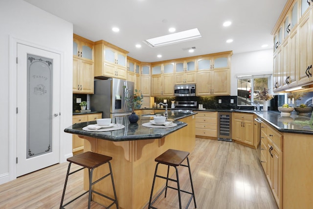 kitchen with a skylight, a center island with sink, stainless steel appliances, beverage cooler, and light hardwood / wood-style flooring