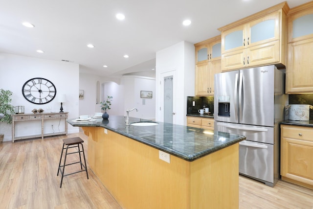 kitchen featuring a center island with sink, stainless steel refrigerator with ice dispenser, light wood-type flooring, dark stone counters, and sink