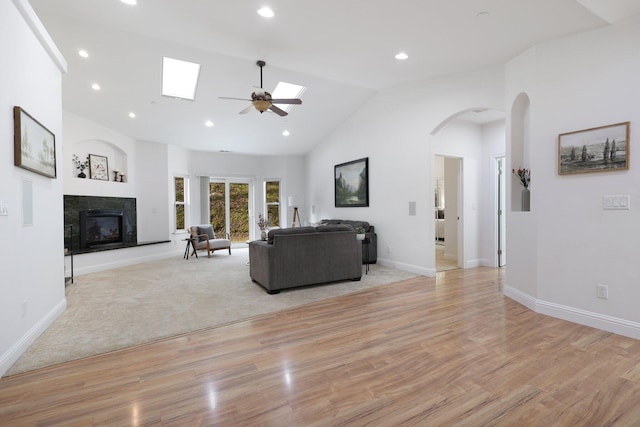 living room featuring ceiling fan, a skylight, light hardwood / wood-style floors, and high vaulted ceiling