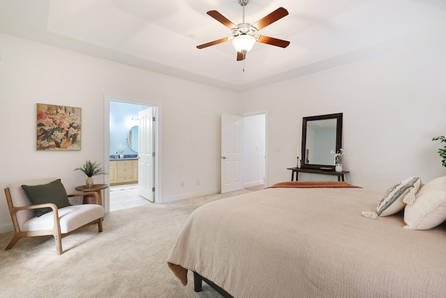 bedroom with ensuite bathroom, light colored carpet, ceiling fan, and a tray ceiling