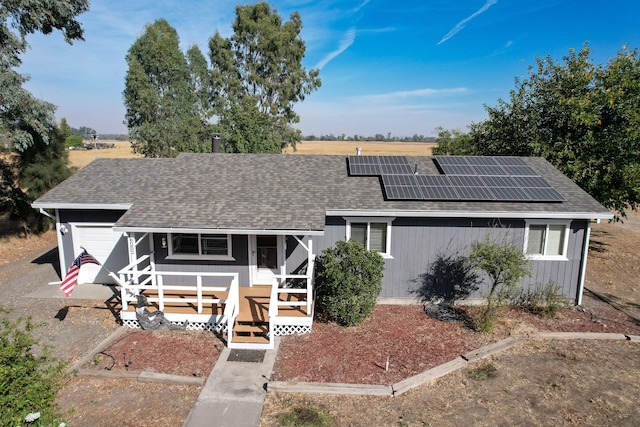 ranch-style home with covered porch, solar panels, a garage, and a wooden deck