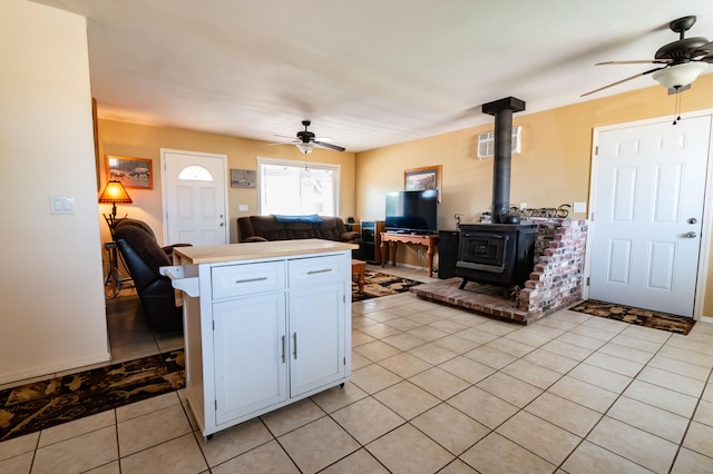 kitchen featuring a wood stove, white cabinets, ceiling fan, light tile patterned floors, and kitchen peninsula