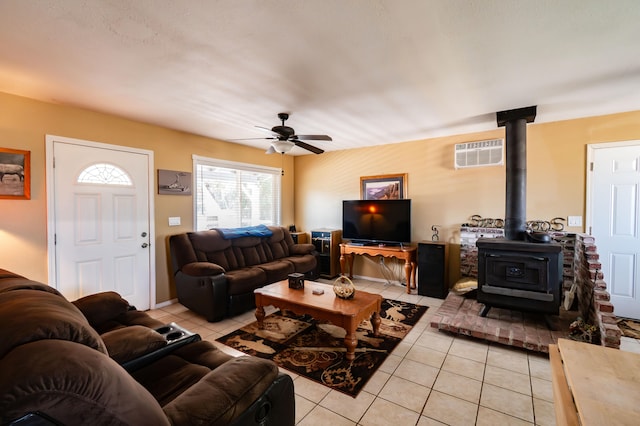 tiled living room with a wall unit AC, a wood stove, and ceiling fan