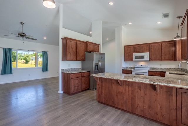 kitchen with white appliances, sink, light hardwood / wood-style flooring, light stone countertops, and decorative light fixtures