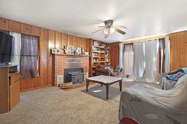 carpeted living room featuring a wood stove, ceiling fan, and wood walls