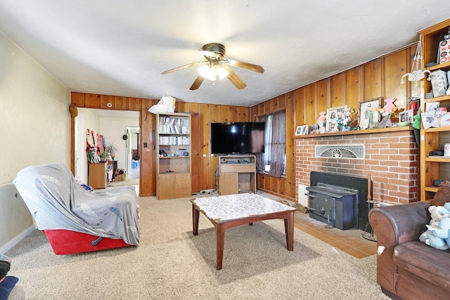 living room featuring light colored carpet, a wood stove, ceiling fan, and wood walls