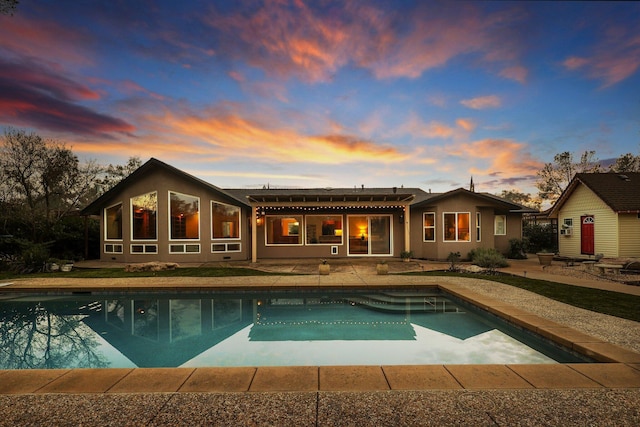 back house at dusk featuring a pergola and a patio