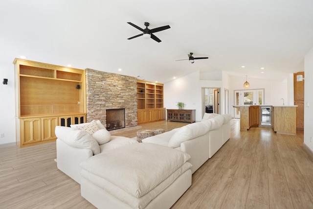 living room with a stone fireplace, vaulted ceiling, built in features, light wood-type flooring, and beverage cooler