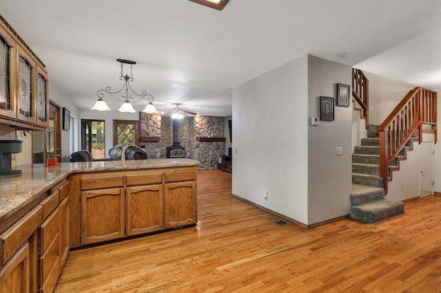 kitchen featuring a wood stove, decorative light fixtures, light hardwood / wood-style flooring, a notable chandelier, and kitchen peninsula