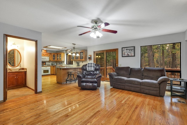 living room featuring ceiling fan with notable chandelier and light wood-type flooring