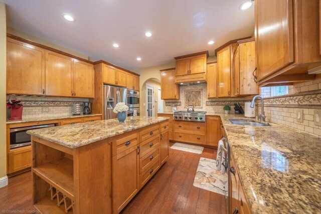 kitchen with light stone countertops, stainless steel appliances, sink, a center island, and dark hardwood / wood-style floors