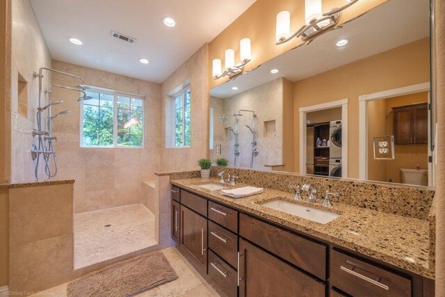 bathroom featuring vanity, tile patterned flooring, toilet, stacked washing maching and dryer, and tiled shower