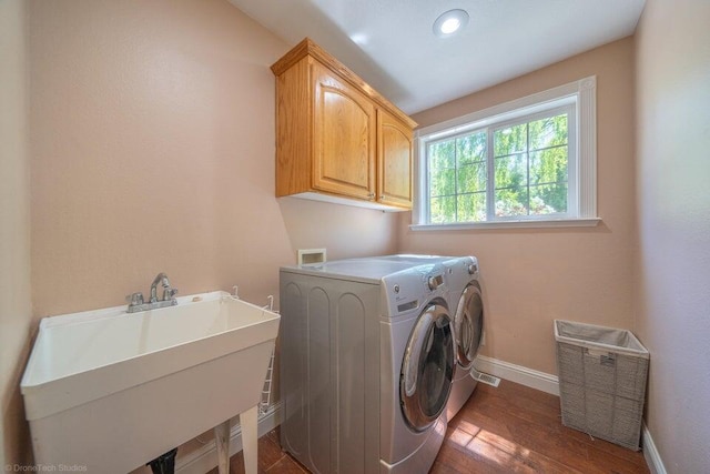 clothes washing area featuring dark wood-type flooring, washer and clothes dryer, cabinets, and sink