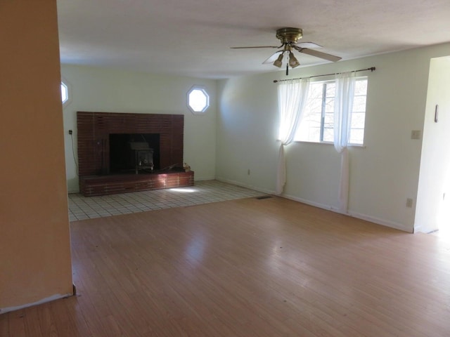 unfurnished living room with light hardwood / wood-style floors, a wood stove, and ceiling fan