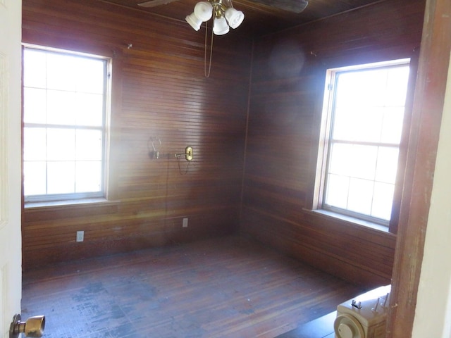 spare room featuring a healthy amount of sunlight, hardwood / wood-style flooring, ceiling fan, and wooden walls