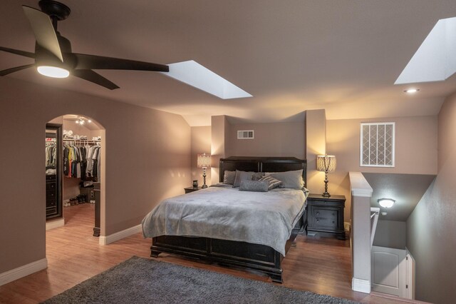 bedroom with ceiling fan, light hardwood / wood-style flooring, a walk in closet, a closet, and vaulted ceiling with skylight