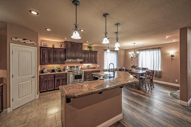 kitchen with hardwood / wood-style floors, a large island with sink, sink, stainless steel range oven, and dark brown cabinetry