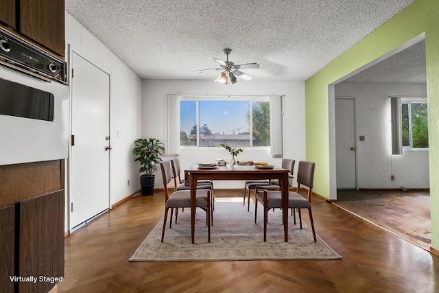 dining space with a textured ceiling, dark parquet floors, ceiling fan, and a healthy amount of sunlight