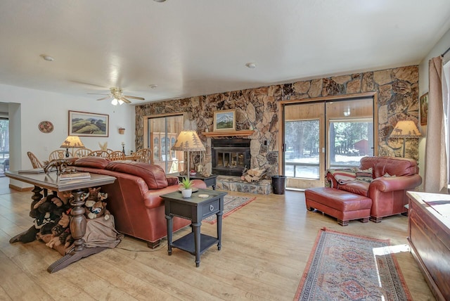 living room with ceiling fan, a stone fireplace, and light wood-type flooring