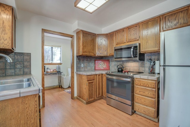 kitchen featuring sink, tasteful backsplash, tile counters, light hardwood / wood-style floors, and stainless steel appliances