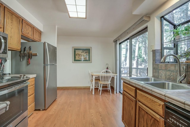 kitchen featuring tile countertops, sink, decorative backsplash, light wood-type flooring, and stainless steel appliances