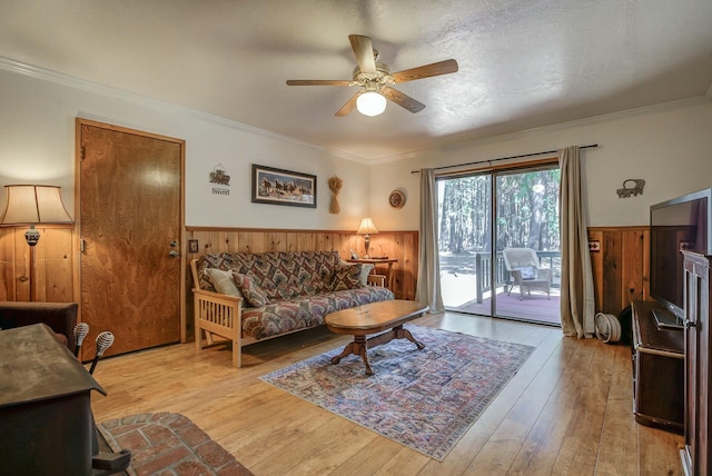 living room featuring wooden walls, light hardwood / wood-style flooring, ceiling fan, and crown molding