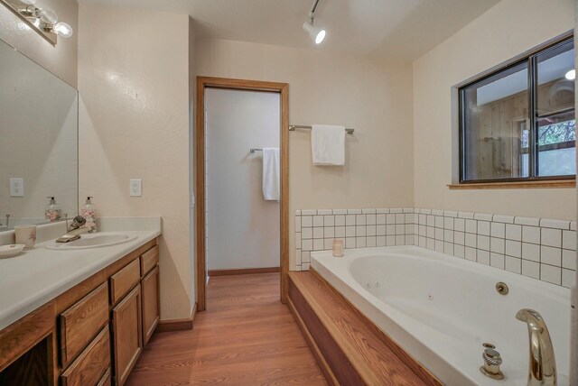 bathroom with hardwood / wood-style floors, vanity, tiled bath, and track lighting