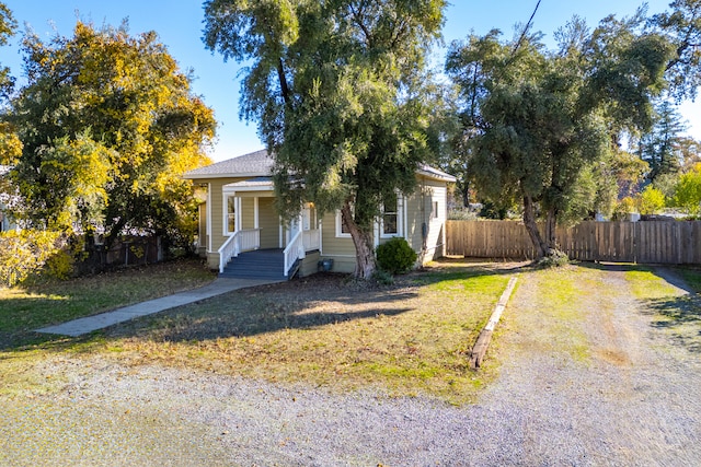 view of property hidden behind natural elements featuring a porch and a front lawn