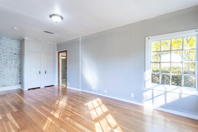 unfurnished bedroom with hardwood / wood-style floors and brick wall